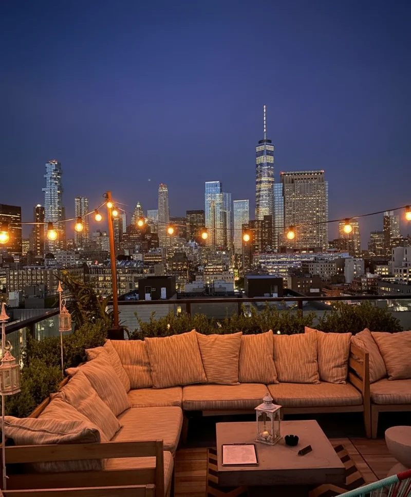 Turn this rooftop photo into a evening time photo, with gradient dark night time sky, background skyscrapers lights up, th...